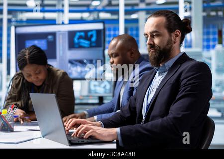 Solar panels manufacturing plant employee using notebook to track energy production and efficiency. Man in photovoltaics factory monitoring system performance on laptop next to colleagues Stock Photo