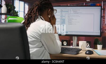 Woman feeling worried while looking at UI on PC screen, having trouble executing programming code. Anxious IT developer concerned by errors popping up while testing code in apartment, camera B Stock Photo