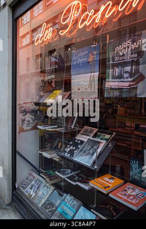 A vibrant bookstore window display in Paris, France, featuring books, posters, and a glowing neon sign. Stock Photo