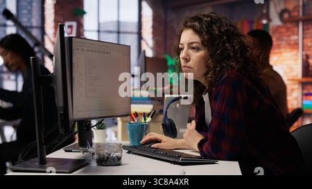 Happy employee using programming languages on PC in IT startup office to build applications. Cheerful IT expert using computer in software development agency to code, camera B Stock Photo