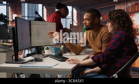 Team of IT specialists using programming languages on PC in startup office to build applications. Teamworking colleagues using computer in software development agency to code, camera A Stock Photo