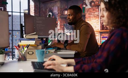Irked man punching startup office desk in frustration struggling to fix application errors. Upset programmer annoyed by computer bugs while coding in software development agency, camera B Stock Photo