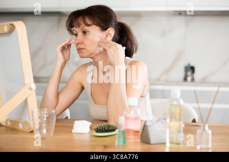 Middle-aged woman examining her facial skin looking in the mirror put on the table Stock Photo