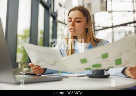 A Young Woman Engaged in Analyzing Business Charts and Data at a Modern Workspace Setting Stock Photo