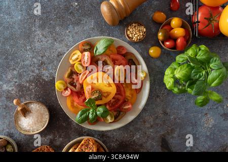 Top view of sliced tomatoes with basil, olives, salt bowl and pepper mill ready for fresh summer salad Stock Photo