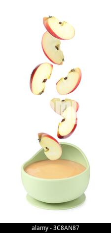 Baby food. Apple slices falling into bowl of puree on white background Stock Photo