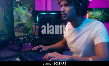 Indian Arabian Latino American man play computer video game monitor championship smiling cyberspace guy headphones technology streamer gamer online Stock Photo