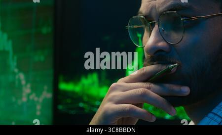 Indian Arabian man programmer coder hacker male guy trader IT specialist thoughtful analyst thinking analysing cryptocurrency financial chart graph Stock Photo