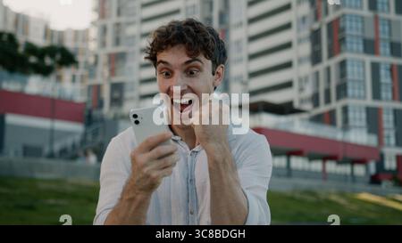 Happy excited Caucasian man holding mobile phone smartphone good news guy winning celebrate success male businessman achievement triumph surprised bet Stock Photo