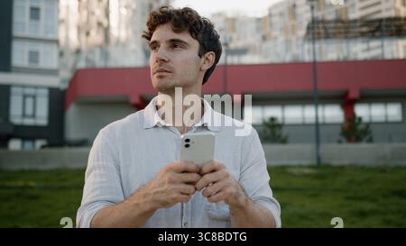 Confident Caucasian young man holding mobile phone smartphone businessman outdoor guy searching location at city looking around town male online Stock Photo