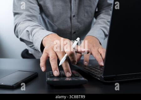 Close-up of man's hands using calculator and typing on laptop keyboard with pen in hand. Concept of financial planning, accounting, budgeting, tax cal Stock Photo