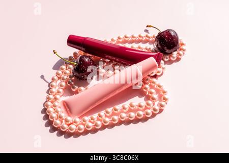 Two tubes with a cosmetic product for lip skin care, balm, mask lie on chic pearl beads with ripe cherries. Natural Care Empty Packaging Layout Stock Photo