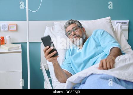 Middle Aged Biracial Man Lying in Hospital Bed Using Smartphone Stock Photo