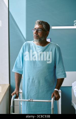 Middle Aged Biracial Man Standing by Window Using Walker during Recovery Stock Photo