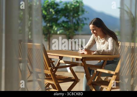 Happy woman using cell phone at home sitting in a terrace outdoors Stock Photo