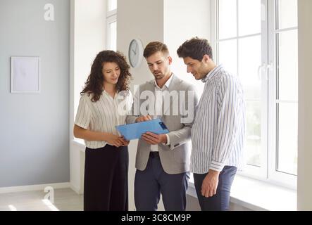 Young couple talking with realtor agent discussing contract standing in modern empty new apartments Stock Photo