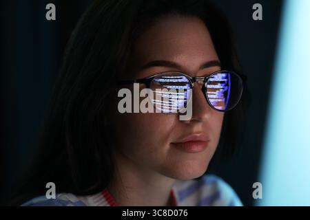 Young woman wearing glasses with reflection on dark background, closeup Stock Photo
