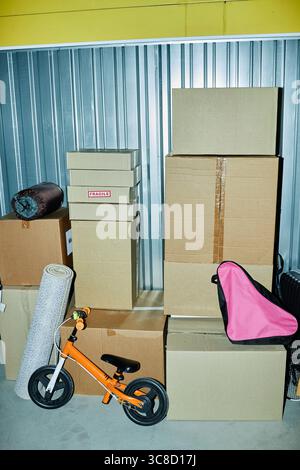 Stacked Cardboard Boxes and Orange Balance Bike in Storage Facility Setting Stock Photo