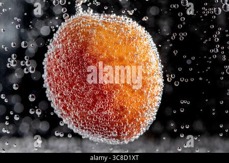 A colorful apricot is immersed in water and covered in bubbles Stock Photo