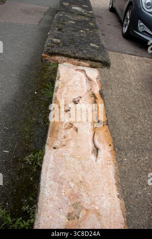 damaged missing low cement wall next to road and a black  parked car Stock Photo