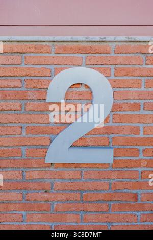 Large Silver Number Two On Traditional Red Brick Wall Of Modern Building. House number, address detail, architectural element, close up view, property Stock Photo