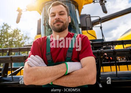 Portrait of farm machinery operator standing confidently in front of combine harvester Stock Photo