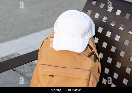 Blank white baseball cap on top of an urban backpack . Template Mock up Stock Photo