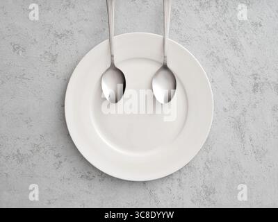 Two spoons are forming a smiling face on a white plate on a gray background, representing happiness and satisfaction with food Stock Photo