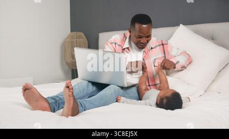 Father Bonding With Baby While Using Laptop on Bed at Home Stock Photo