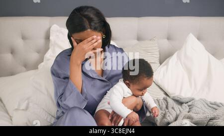Postpartum Depression, Stressed Mother Sitting on Bed with Her Baby, Reflecting in an Emotional Moment Stock Photo