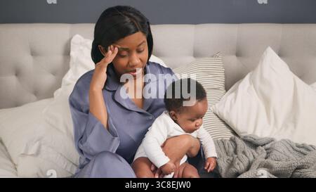 Postpartum Depression, Stressed Mother Sitting on Bed with Her Baby, Reflecting in an Emotional Moment Stock Photo