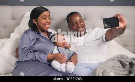 Happy Family Taking a Selfie Together on a Comfortable Bed in Their Home Stock Photo