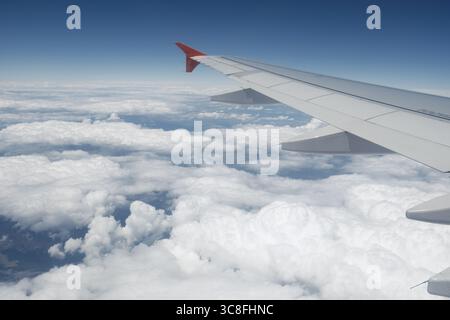A peaceful in-flight view from a passenger seat showing an aircraft wing soaring above soft clouds under a bright blue sky. Stock Photo