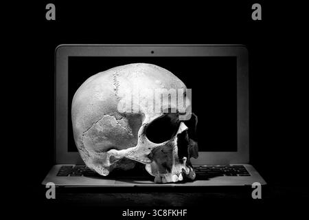 Cybercrime or hacking concept. Laptop in dark room under beam of light with a skull. Idea of virus or worm program cyber attack Stock Photo