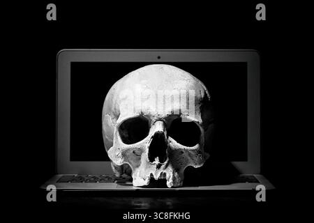 Cybercrime or hacking concept. Laptop in dark room under beam of light with a skull. Idea of virus or worm program cyber attack Stock Photo