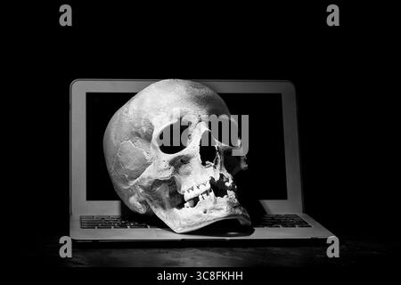Cybercrime or hacking concept. Laptop in dark room under beam of light with a skull. Idea of virus or worm program cyber attack Stock Photo