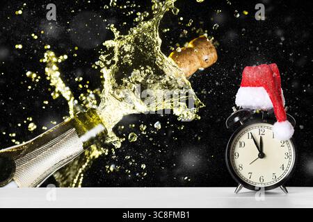 Christmas or New Year celebration theme with explosion of splashing champagne sparkling wine near vintage alarm clock with Santa Claus hat against dar Stock Photo