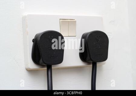 UK switched double electric wall socket with two black plugs. Stock Photo