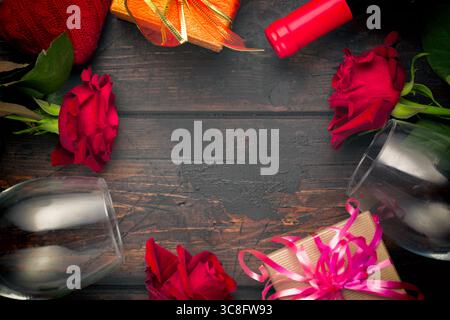 Valentines day romantic greeting card. Red rose flowers, wine bottle, two glasses and gift boxes on wooden table. Free space Stock Photo