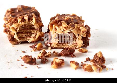 two broken chocolate wafer caramel bars sprinkled with peanuts isolated on white background. Stock Photo