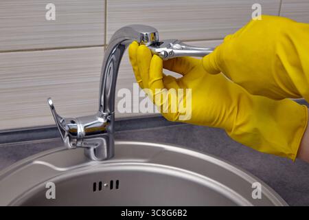 hands in yellow rubber gloves repairing a water faucet with an adjustable wrench. Stock Photo