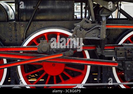 Close-up of steam locomotive driving mechanism, revealing intricate red and white wheels with connecting mechanical components Stock Photo