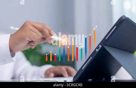 Financial growth, data analysis, strategic planning, and technology concept. Businessman hand using stylus on tablet with colorful digital bar graph a Stock Photo