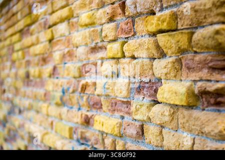 Weathered brick wall presenting yellow and orange tones, revealing intricate surface details from close perspective Stock Photo