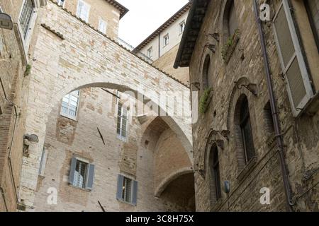Archway connecting two historical buildings in Perugia, Italy, featuring ancient stone walls and windows with shutters Stock Photo