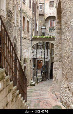 Historic narrow alleyway in Perugia, Italy, featuring stone buildings, an arched bridge, and street art on the walls Stock Photo