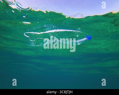 Discarded plastic bottle floating beneath the surface of the sea, symbolizing ocean pollution and environmental impact of plastic waste. Selective foc Stock Photo