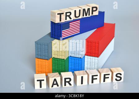 Wood cubes with Trump Tariffs words over containers with flag of US. Concept for new tariffs imposed by US President Donald Trump. Stock Photo