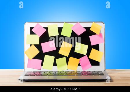 Many blank sticky notes covering modern laptop screen on wooden table against blue background. Concept of deadlines or ideas Stock Photo