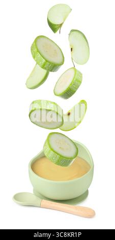 Baby food. Zucchini and apple slices falling into bowl of puree on white background Stock Photo
